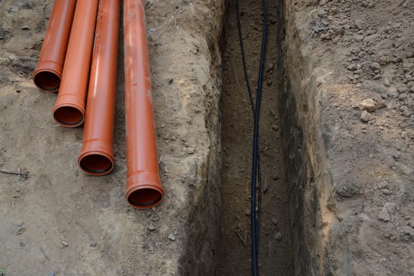 Safety,Supply,To,House,New,Insulated,Internet,,Gas,Cord,,Red Safety supply to house new insulated internet, gas cord, red metal-plastic tap system construction lay in pit dug in garden. Top view with space for text on grey clay earth. Telecom service industry